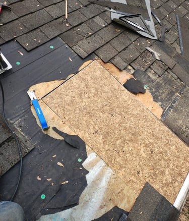 Roofing contractor replacing damaged asphalt shingles and repairing wood roof decking with tools.