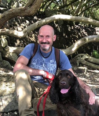 Smiling man with a brown spaniel sitting under a tree