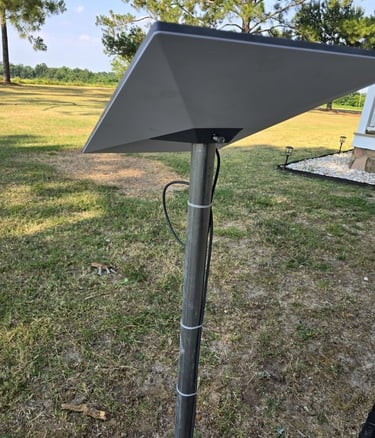 A Starlink satellite internet dish mounted on a metal pole in a grassy backyard.