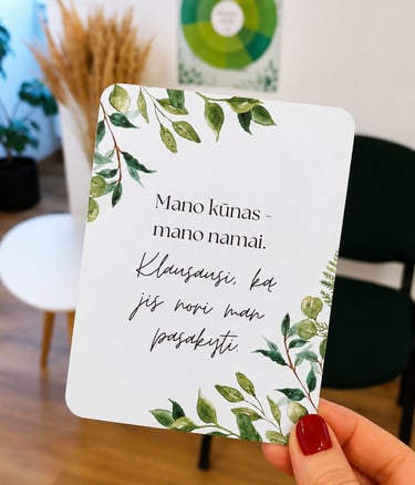 Afirmacijos kortelė, laikoma rankoje. Joje pateikiama afirmacija apie kūno priėmimą.