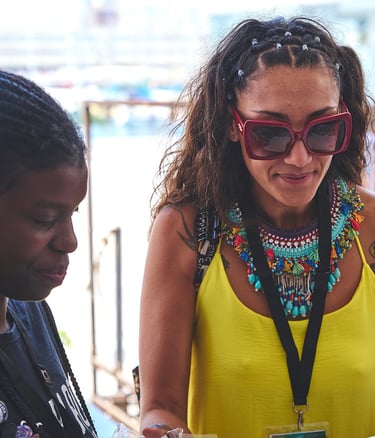 Una mujer afro al lado de otra con vestido amarillo gafas de sol y collar afro grande