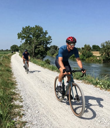 Cyclist on a gravel bike riding along a sunlit country road lined with vineyards.