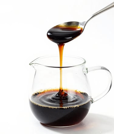 Golden honey dripping from a spoon into a glass pitcher isolated on white.