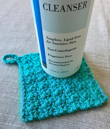 Bottle of cleanser on top of a aqua crocheted square face scrubbie
