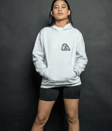 Una joven vistiendo una sudadera blanca con estampado gráfico y shorts, posando en fondo gris.