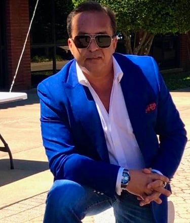 Bedig Minassian, the brand's founder, sits on a bench in a blue suit and sunglasses