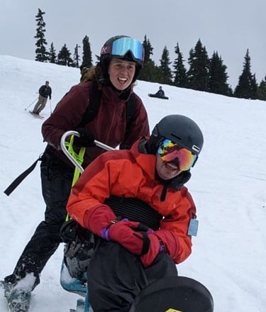Sean in the sit ski and Jacqueline holding the back skiing downhill with big smiles