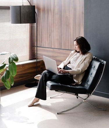 A woman sitting in a black chair typing on a laptop
