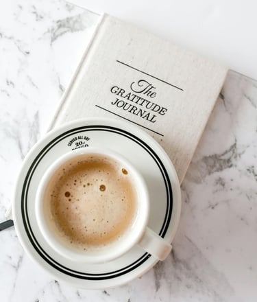 a frothy cup of coffee and a gratitude journal on a marble table