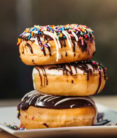 three stacked donuts with white glaze and chocolat coat and colorful sprinkles