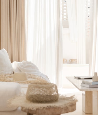 Linen curtains filtering direct midday light onto a plaster wall.
