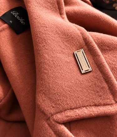 Rectangular metal logo plate attached to a coral wool coat