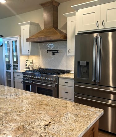 Kitchen island with granite countertop, steel refrigerator, and gas stove hood - Saddle Horn Custom