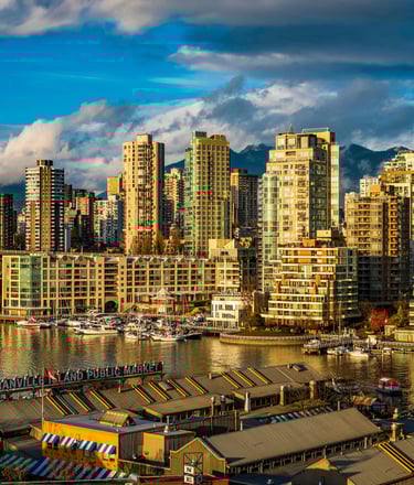 A wide panoramic view of the same waterfront city, with bridges, yachts, and a vibrant skyline under partly cloudy skies.