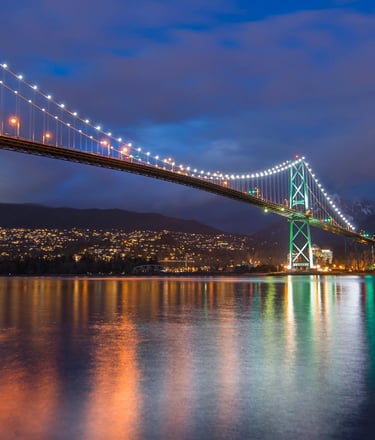 Lions Gate Bridge at night with lights reflecting on the water.