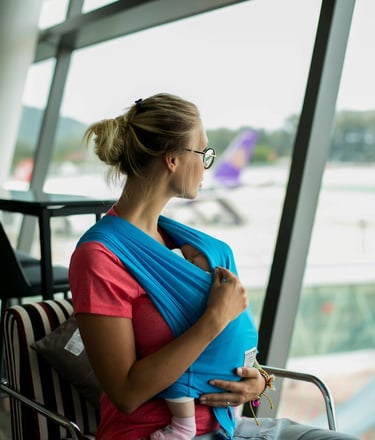 A woman sits in an airport lounge holding a baby in her arms while waiting near the boarding area