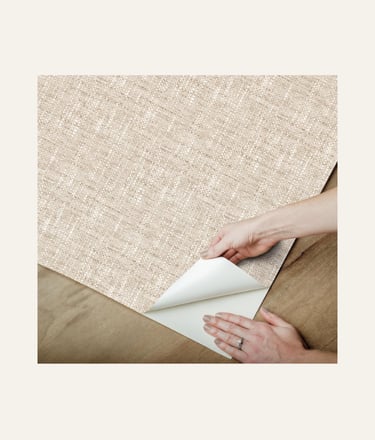 Hands applying beige grasscloth peel and stick textured wallpaper to a surface, showcasing easy DIY home decor updates.