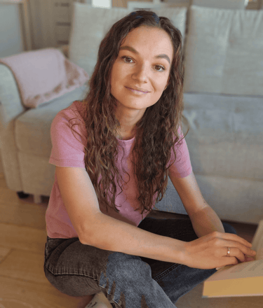 Psichologė Irma Chmieliauskienė. Tamsiaplaukė moteris sėdinti ant grindų su atversta knyga