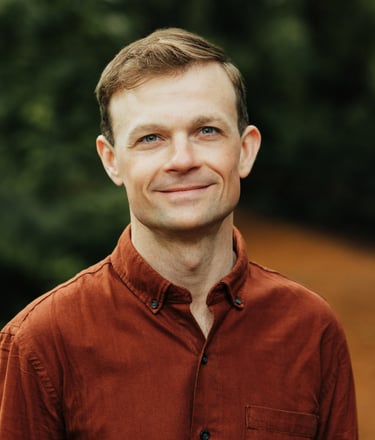 Headshot of Jesse Robertson wearing an orange collared shirt with a forested background.