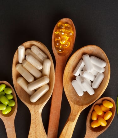 Variety of herbal supplements and vitamin capsules in wooden spoons on a dark background.