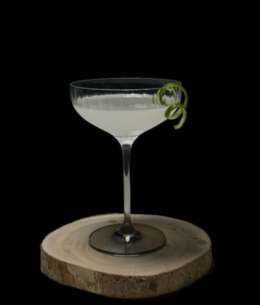 Elegantiškas kokteilis taurėje su laimo žievele, pateiktas ant natūralaus medžio pagrindo.