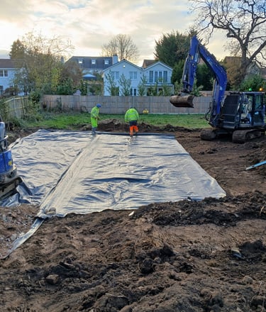Construction workers laying a damp proof membrane on a residential building site with a blue excavator.