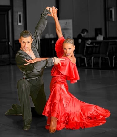A man in a black satin shirt is kneeling with a woman in a red satin dress on the dance floor