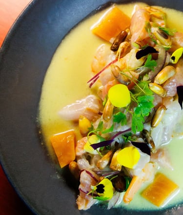 Ceviche Nikkei com peixe branco, camarão, milho crocante, batata-doce e flores comestíveis em um prato fundo escuro