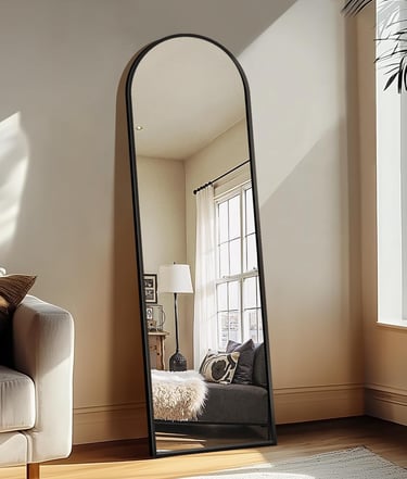 Full-length black arched floor mirror leaning against a wall in a sunlit modern living room.