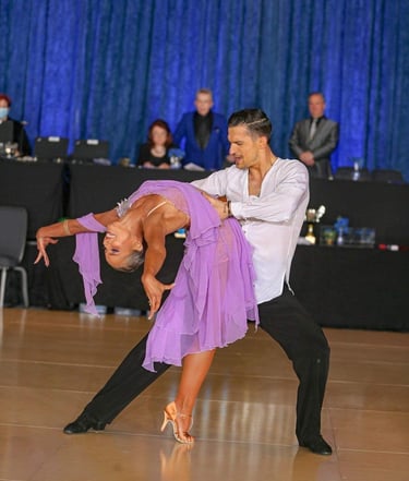 A man in a white silk shirt holds a woman as she arches her back, wearing a purple silk dress