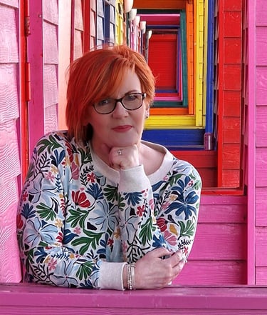 Dawn Vincent Celebrant smiling leaning on brightly coloured beach huts