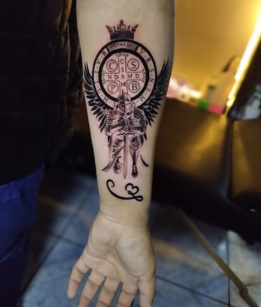 Tatuaje detallado en tinta negra en el antebrazo que presenta una medalla de San Benito: