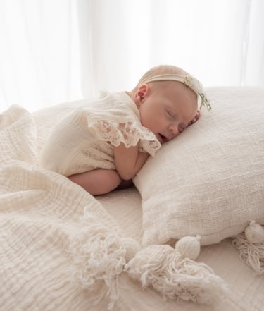 A sleeping newborn girl in a lace romper and flower headband during a professional lifestyle photography session.