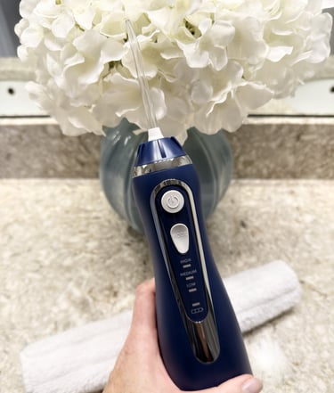 Christine holding a cordless water flosser with flowers and bathroom counter visible in background