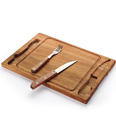Wooden carving board with a stainless steel steak knife and fork set on a white background.