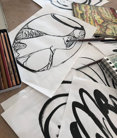 A display of black ink drawings with a vase sketch on top, pencils and notebook