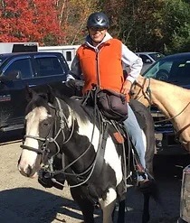 a woman in a vest and hat riding a horse