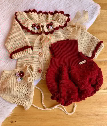 Handmade crochet baby outfit featuring a cream cardigan with floral collar, red bloomers, and a matching bonnet.
