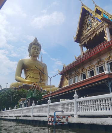 Giant golden Buddha statue at Wat Paknam Phasi Charoen temple seen from a canal in Bangkok, Thailand.