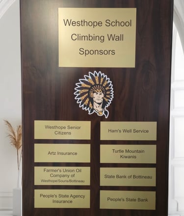 A sponsor plaque hanging on a wall showing school and sponsor names