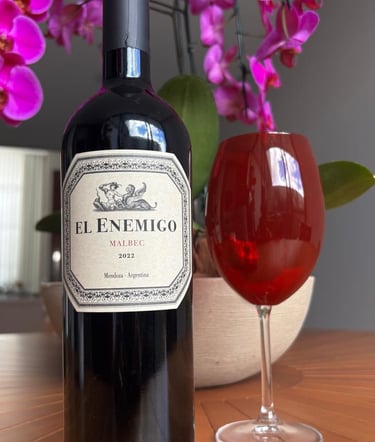 Garrafa de vinho El Enemigo Malbec 2022 ao lado de uma taça de vinho tinto decorada com orquídeas