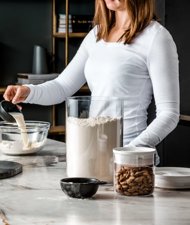 Food product photography - a woman in a white shirt pouring milk in a bowl of flour