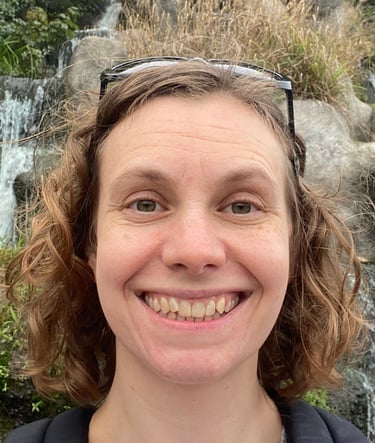 a woman with sunglasses and a backpack standing in front of a waterfall