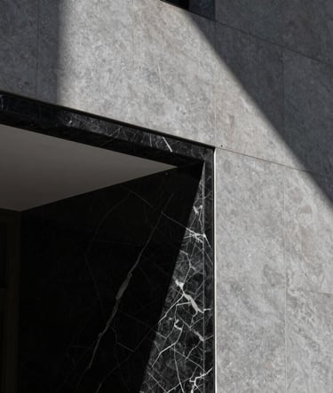 A minimalist architectural detail shot of a Sydney luxury hotel lobby. Focus on premium textures like black marble and grey stone, with a sharp contrast between light and shadow. The lighting is dramatic and cinematic.