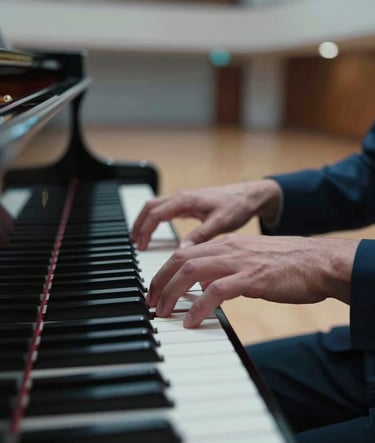 A close-up photograph of hands playing a grand piano in a modern concert hall in a Latin American / Spanish city. The lighting is cinematic with Muted Blue and Dark Navy tones, focusing on the movement and the keys.