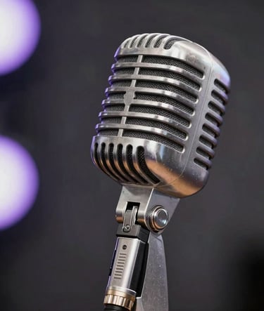 A close-up photograph of a professional vintage silver microphone on a stand. The background is a soft blur of dark charcoal and pale lavender stage lights. Artistic elegance, professional music photography style.