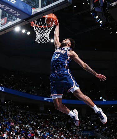 A low-angle wide shot of a professional basketball player in mid-air during a dunk, captured in a North American arena. The background is dark midnight black with dramatic steel blue spotlights. The player's motion is perfectly frozen, showing immense power and speed. Cinematic, high-tech lighting.