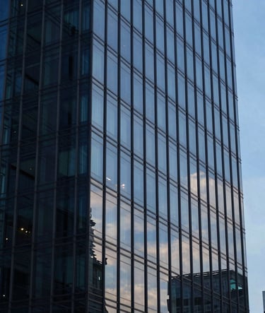 A close-up shot of a modern glass office building in a Southeast Asian / Indonesian city during the blue hour. The reflections on the glass show Dark Navy Blue and Soft Sky Blue tones, conveying professional excellence and quiet competence.
