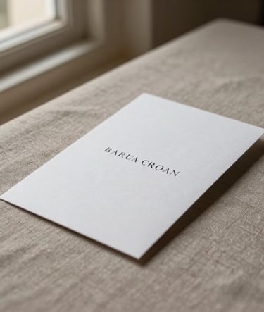 A professional minimalist photograph of an elegant white invitation card resting on a warm taupe linen surface. Soft side lighting from a window, creating a serene and refined atmosphere in a Spanish setting.