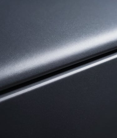 A close-up photograph of a sleek, dark metallic texture with soft light skimming the surface, suggesting premium technology and industrial design, sophisticated slate gray and navy palette.